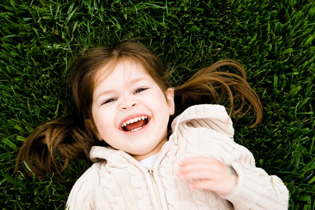 CommunityAd Trades - Charities - girl smiling while laying on grass for Children's Mental Health Week