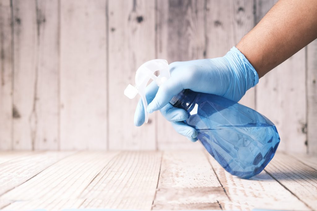 CommunityAd Trades - Cleaning Services - viral cleaning hacks - person wearing a glove using a spray bottle on wooden surface